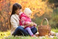 Kid and mother sit with apples basket outdoors in autumnal park Royalty Free Stock Photo